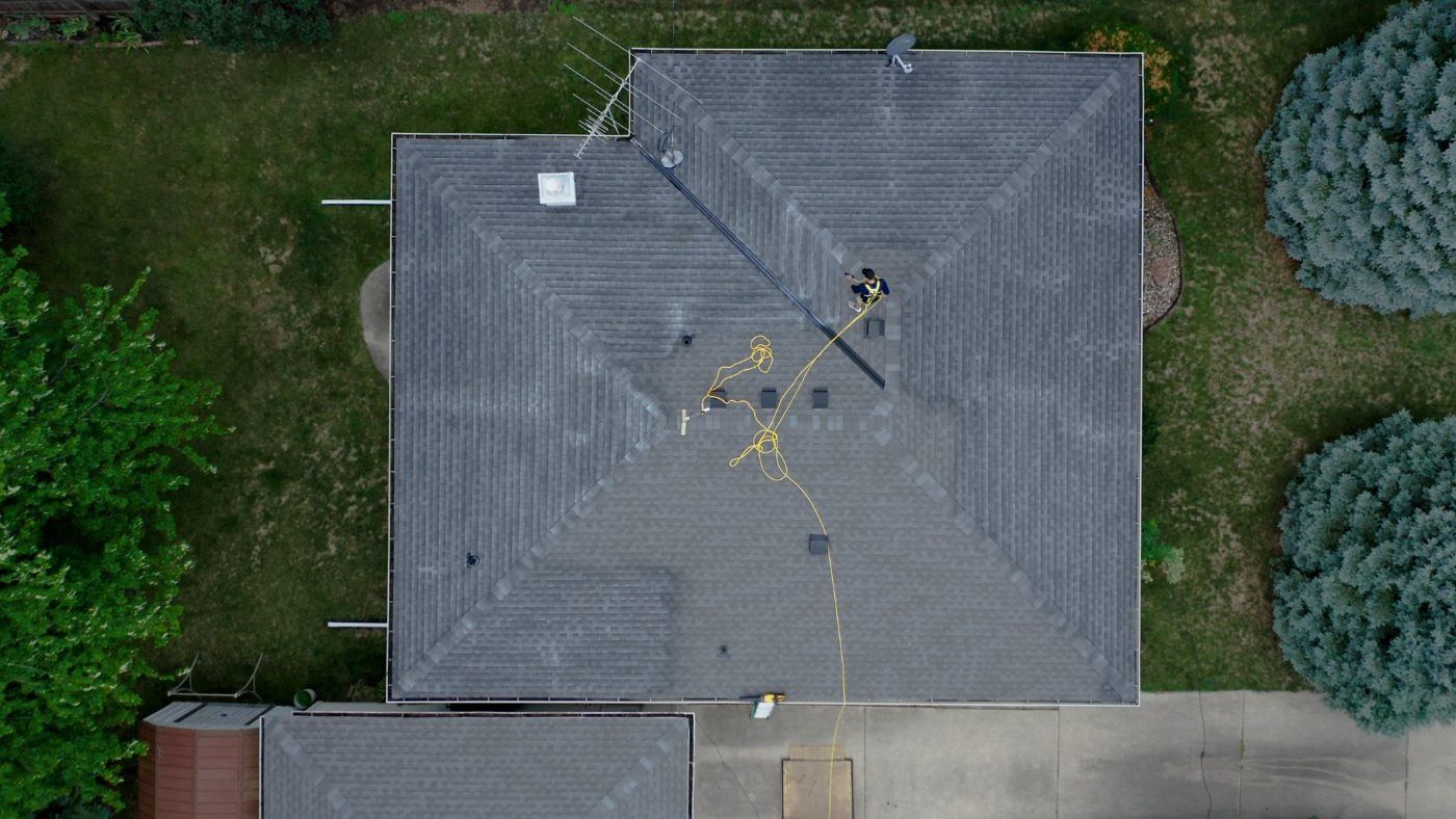Aerial view of an applicator treating a hip roof, with the treated sections darker