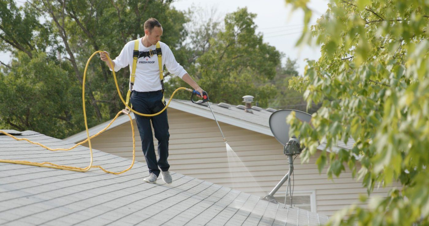 Applicator in a safety harness spraying the treatment across a shingle roof